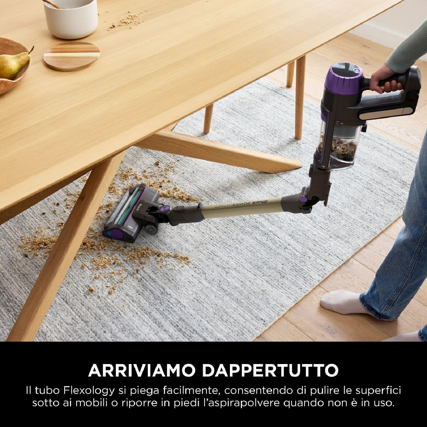 Una persona che aspira un tappeto con un aspirapolvere. L'aspirapolvere è viola e nero. C'è un tavolo.