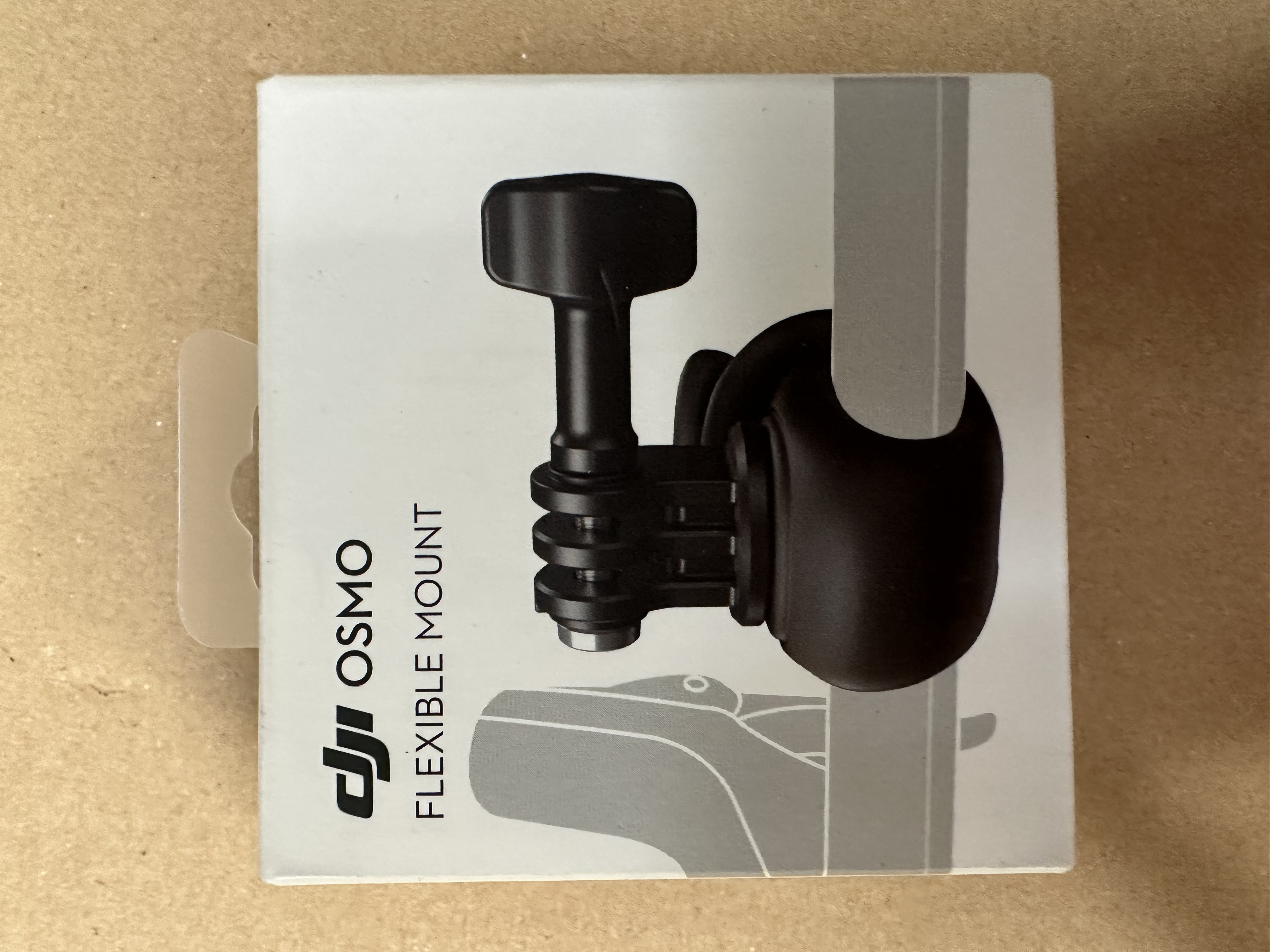 Pudełko do elastycznego mocowania DJI Osmo, białe z ilustracją produktu i tekstem, na brązowej powierzchni.
