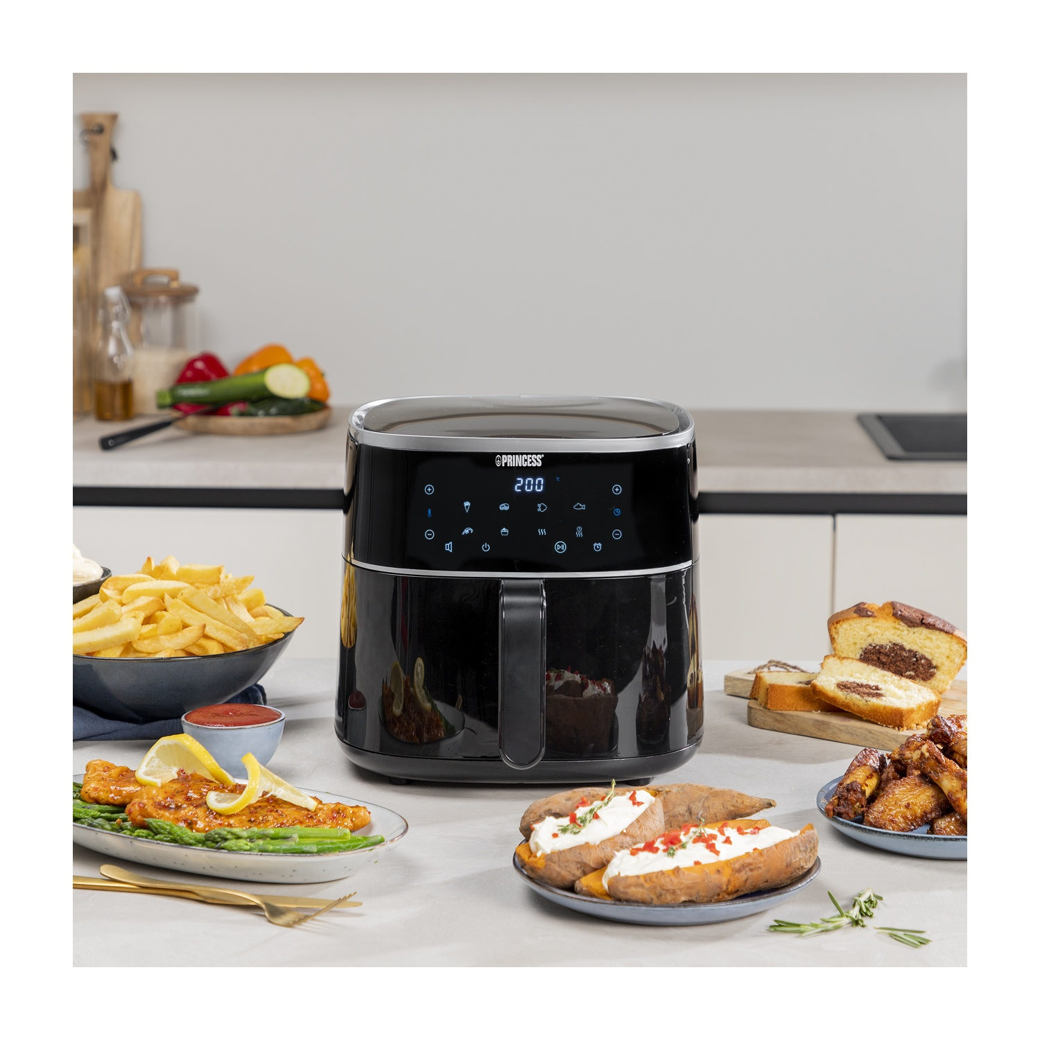Una friggitrice ad aria con vari piatti cotti: patatine fritte, ali di pollo, patate al forno e una torta.