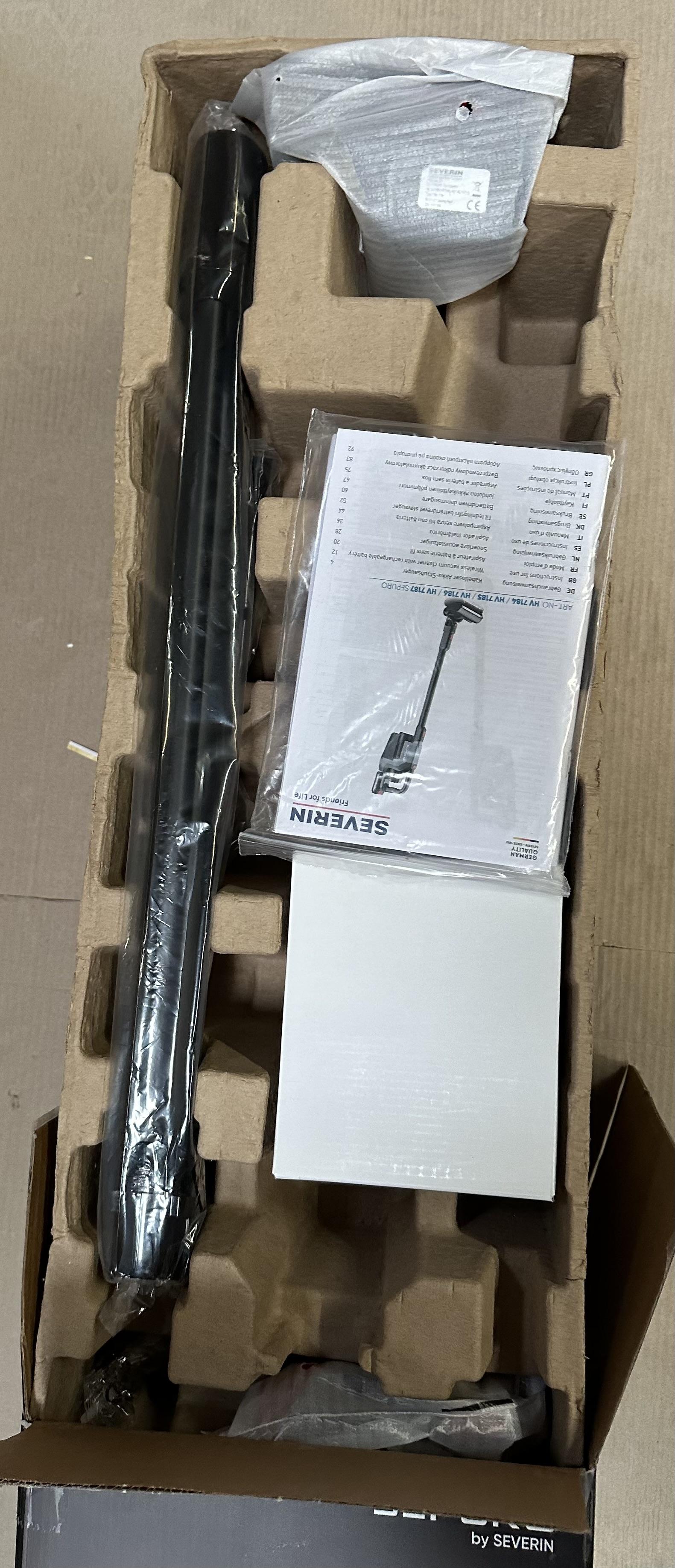 Części odkurzacza w pudełku. Instrukcja, długa czarna rura i inne elementy.