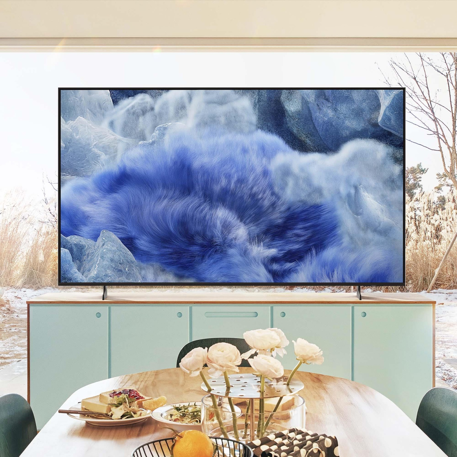 TV che mostra un'immagine astratta blu e soffice. Interno con tavolo, fiori e mobile.