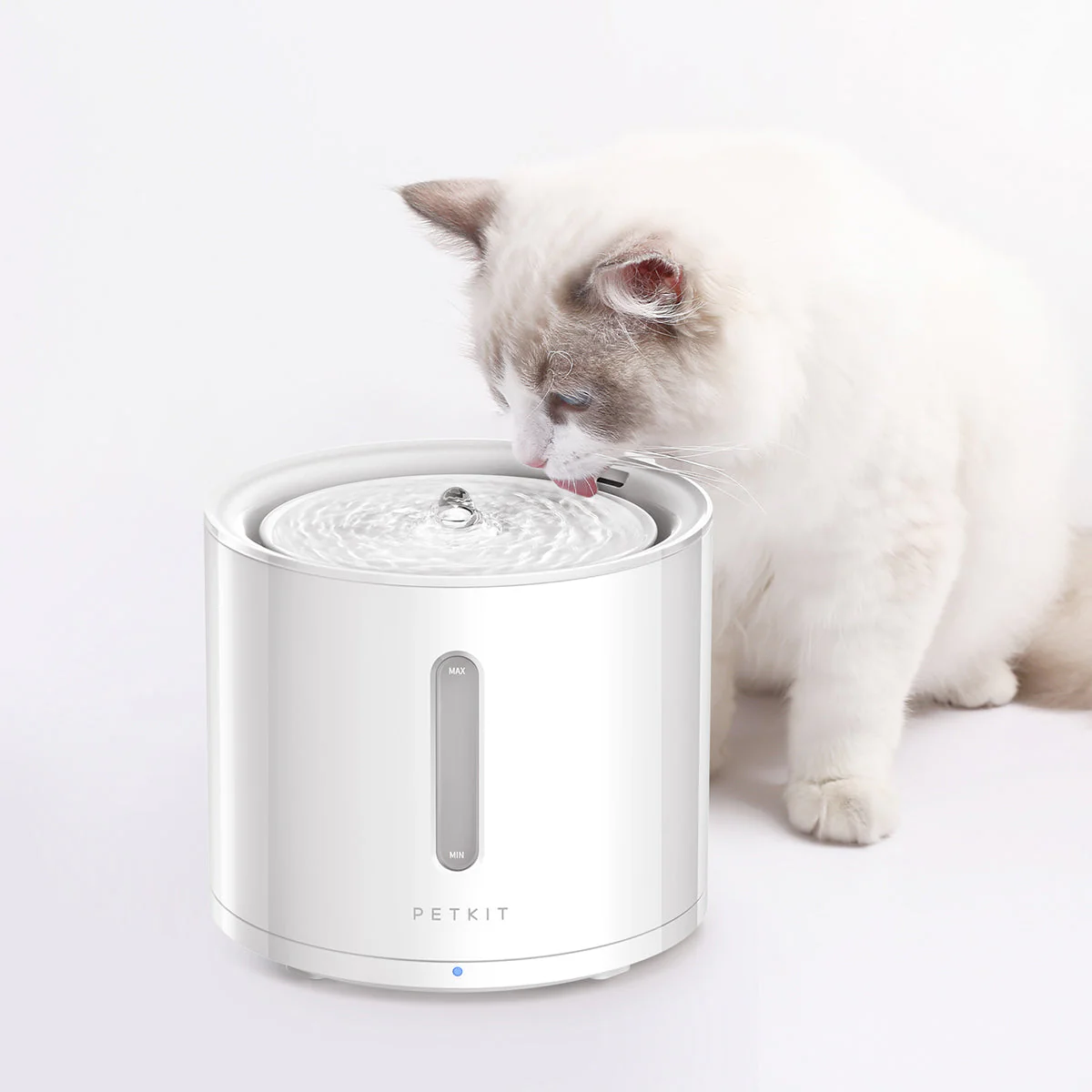 Gatto bianco che beve da fontana per animali bianca con indicatore livello, su sfondo bianco.