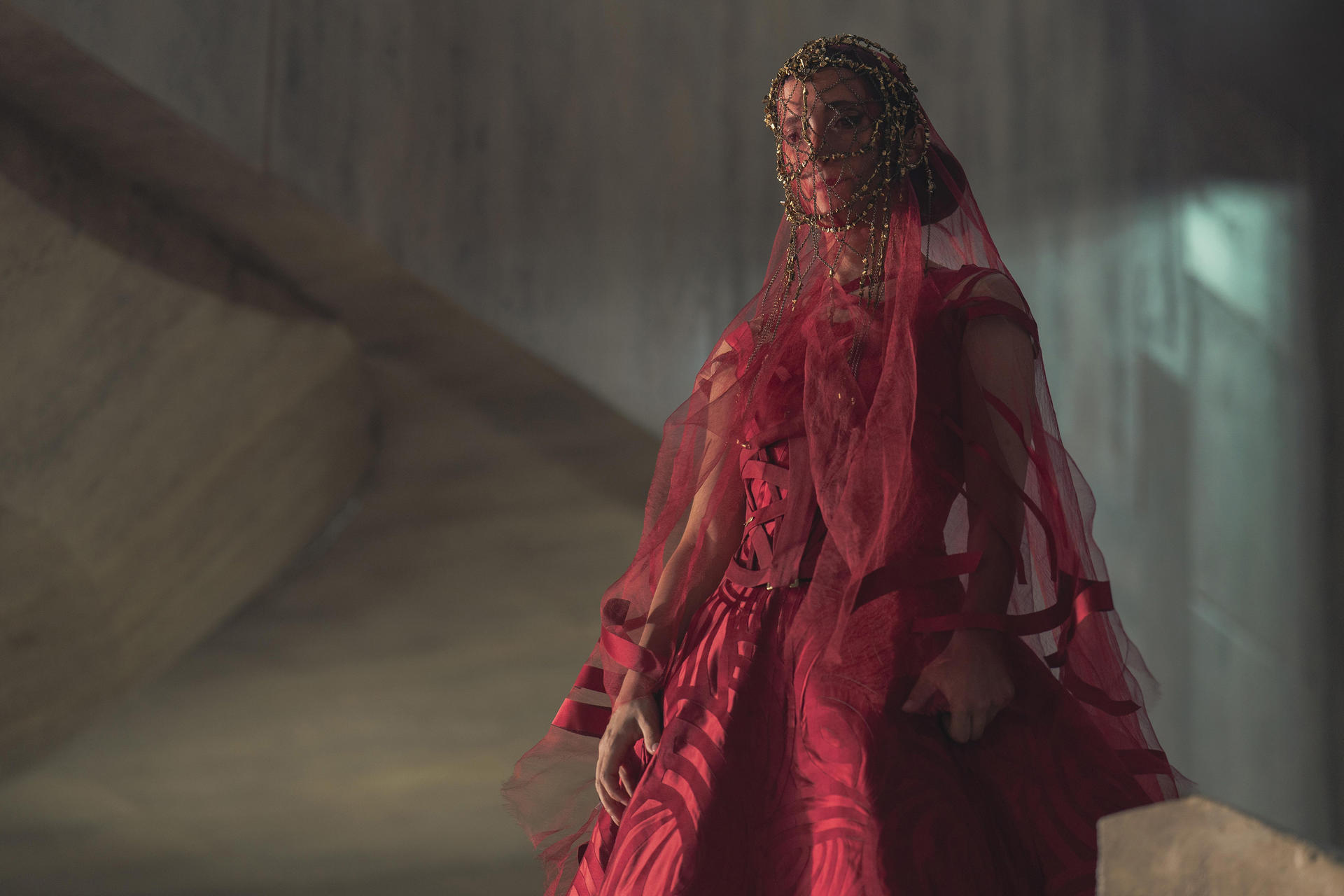 Frau in rotem Kleid mit Schleier, in einer Betonstruktur mit Schatten.