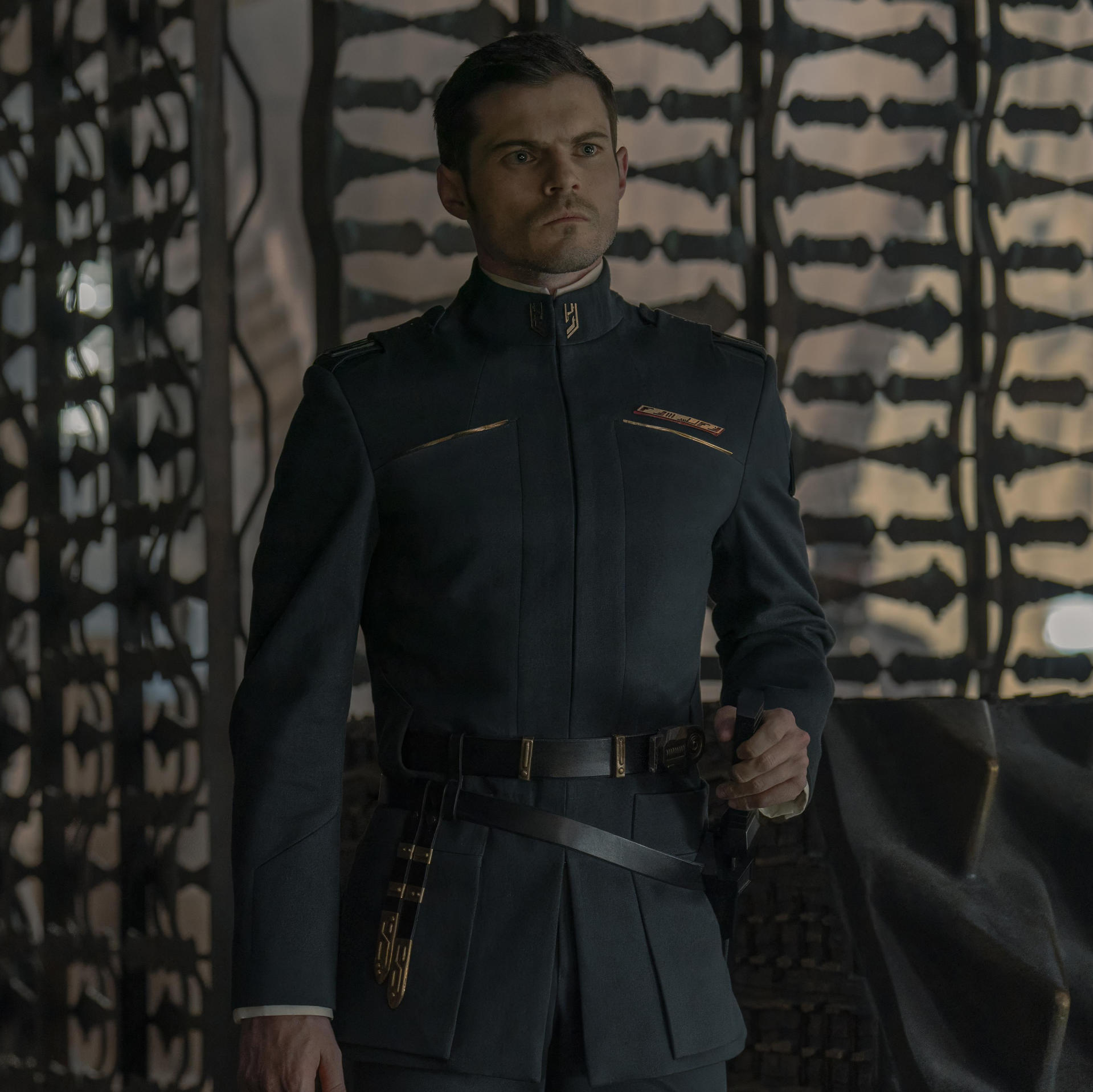 Mann in dunkelblauer Uniform. Hält einen kleinen Gegenstand. Ernsthafter Ausdruck.