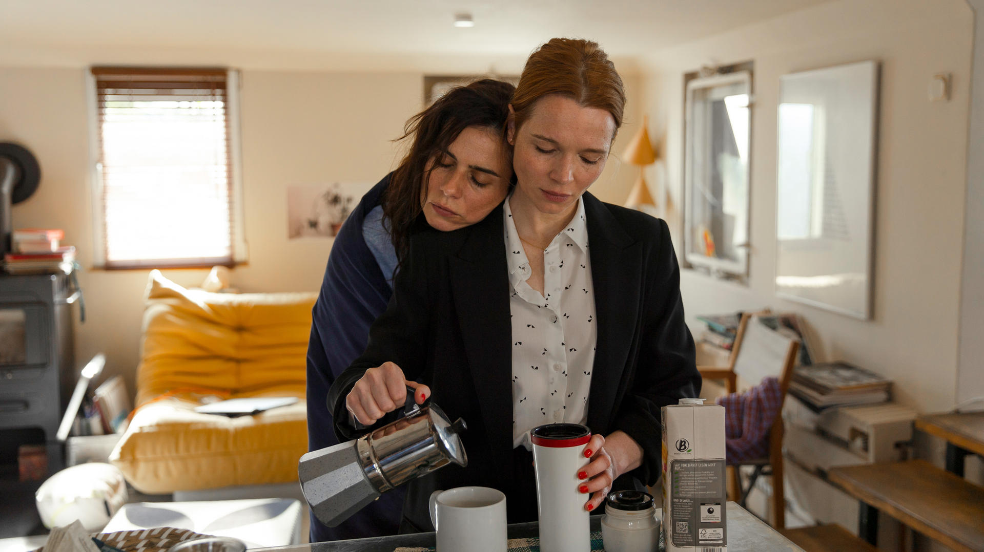 Zwei Frauen, eine gießt Kaffee ein, die andere legt den Kopf an die Schulter.