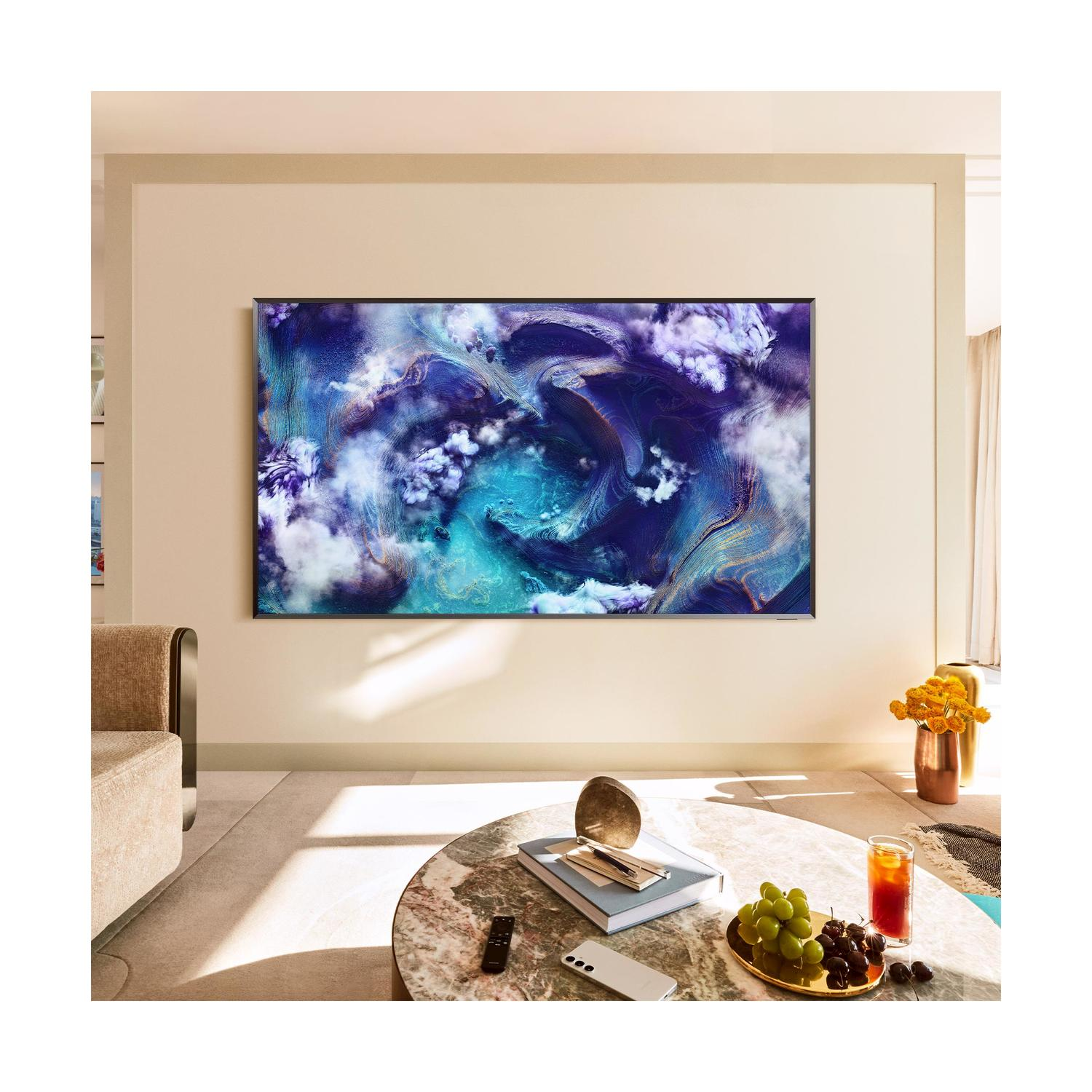 Una grande TV su un muro, che mostra un dipinto astratto colorato, con un tavolo e oggetti davanti.