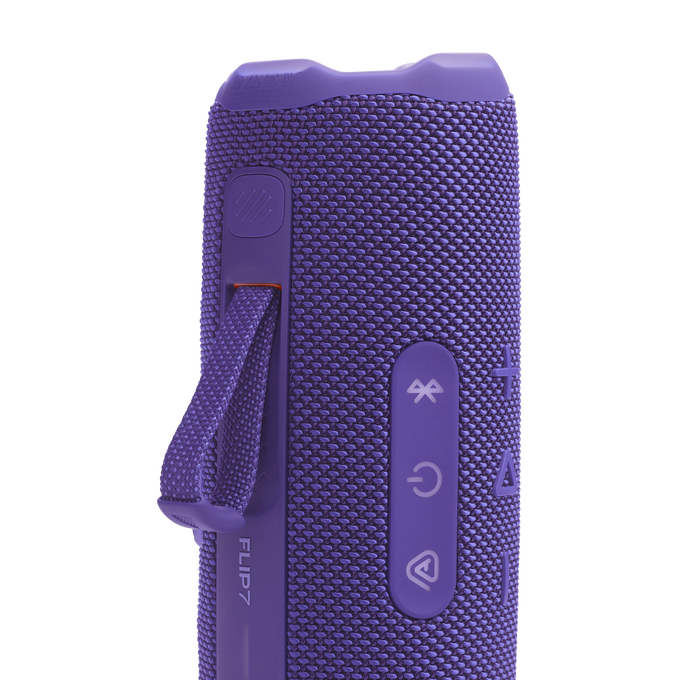 Primer plano de un altavoz JBL Flip 7 morado, mostrando botones de control y una correa. El altavoz tiene una textura de malla.
