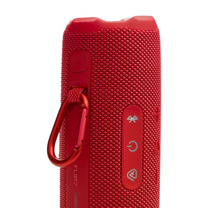 Un altavoz cilíndrico rojo con botones, un cordón y el texto 'FLIP7'.
