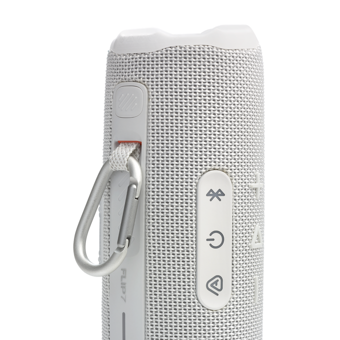 Un altavoz blanco JBL Flip 7 con botones de control y un mosquetón plateado.