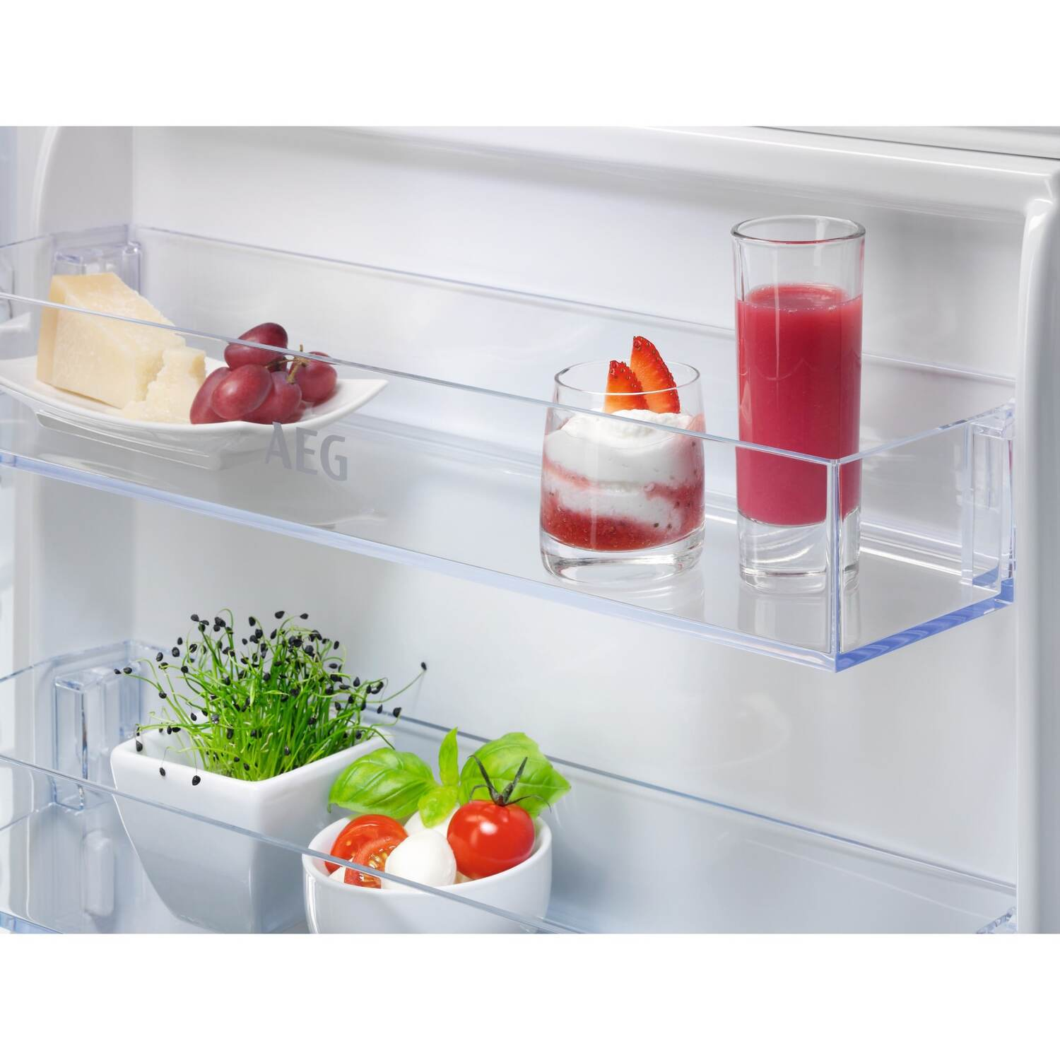 Étagères de réfrigérateur avec aliments : fromage, raisins, dessert aux fraises et un verre de jus. Aussi basilic et tomates.