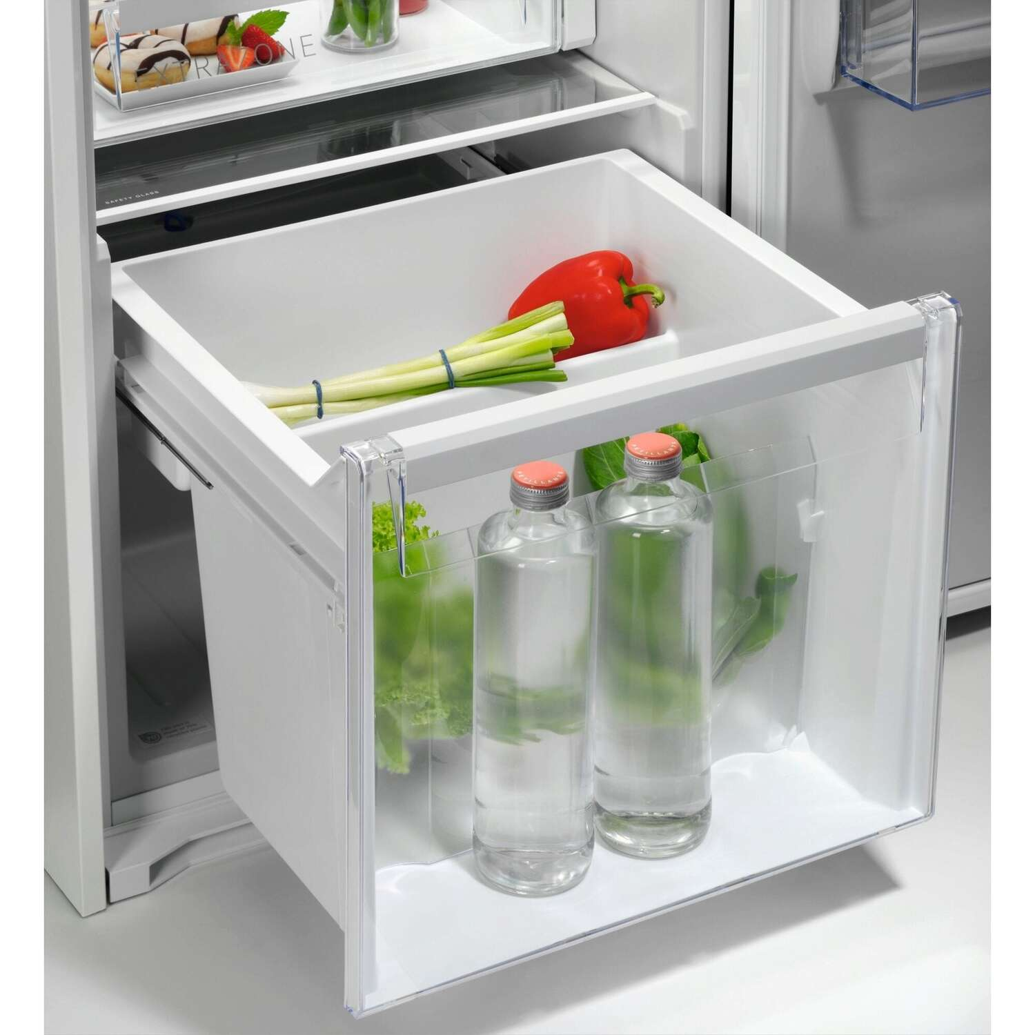 Tiroir de réfrigérateur avec légumes et bouteilles d'eau. Intérieur transparent et blanc.
