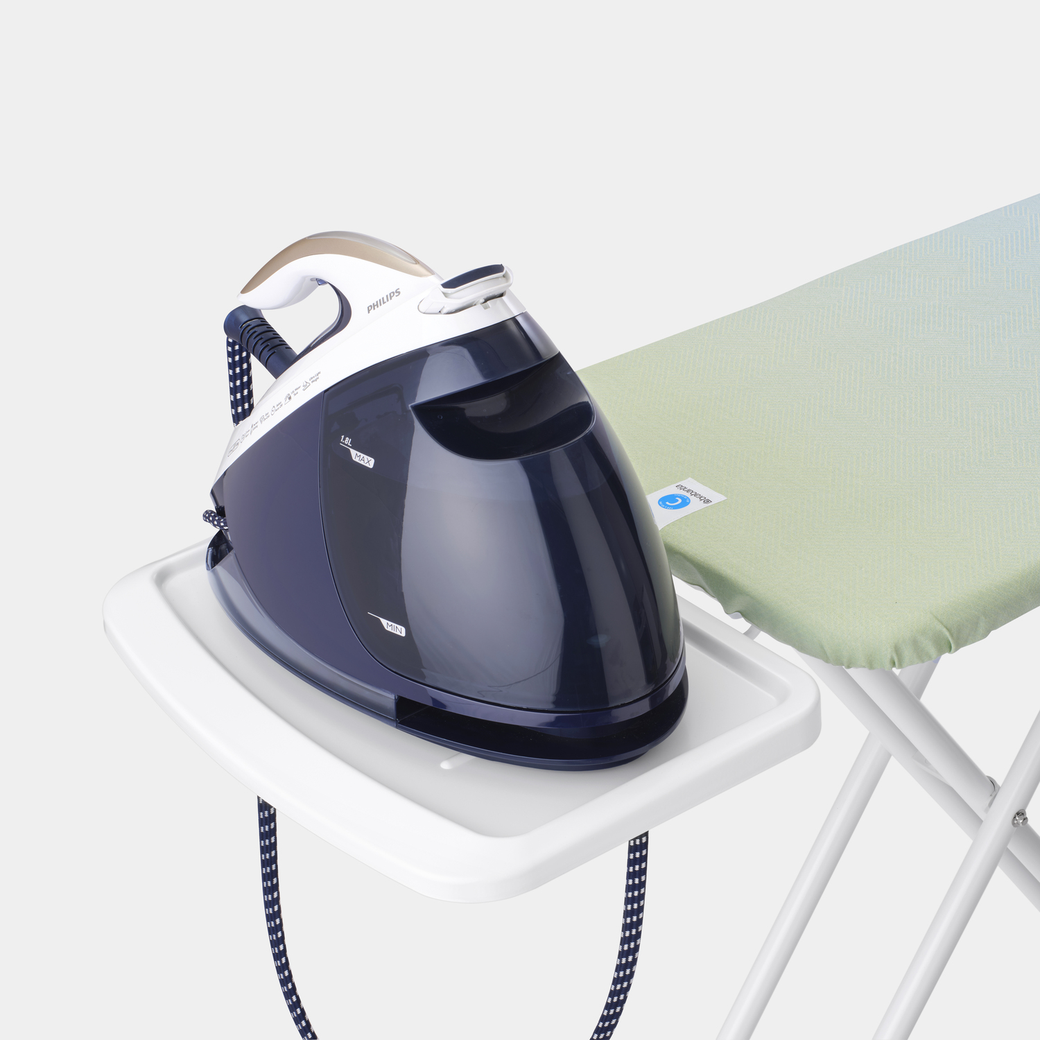 A steam iron on a tray, next to a green and white ironing board.