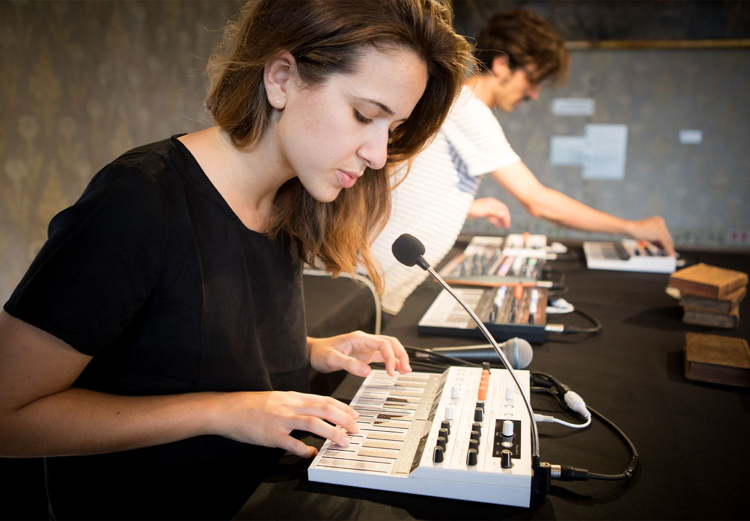 Femme jouant d'un clavier, avec une autre personne en arrière-plan. Table sombre, instruments et cadre de studio.