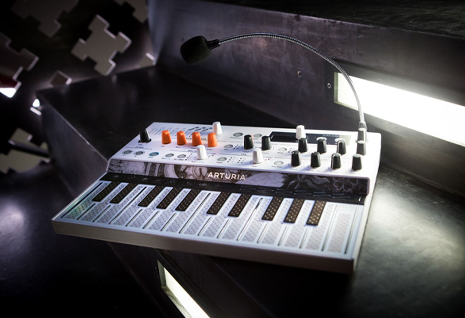 Synthétiseur avec touches, boutons et micro. Accents blancs et oranges.
