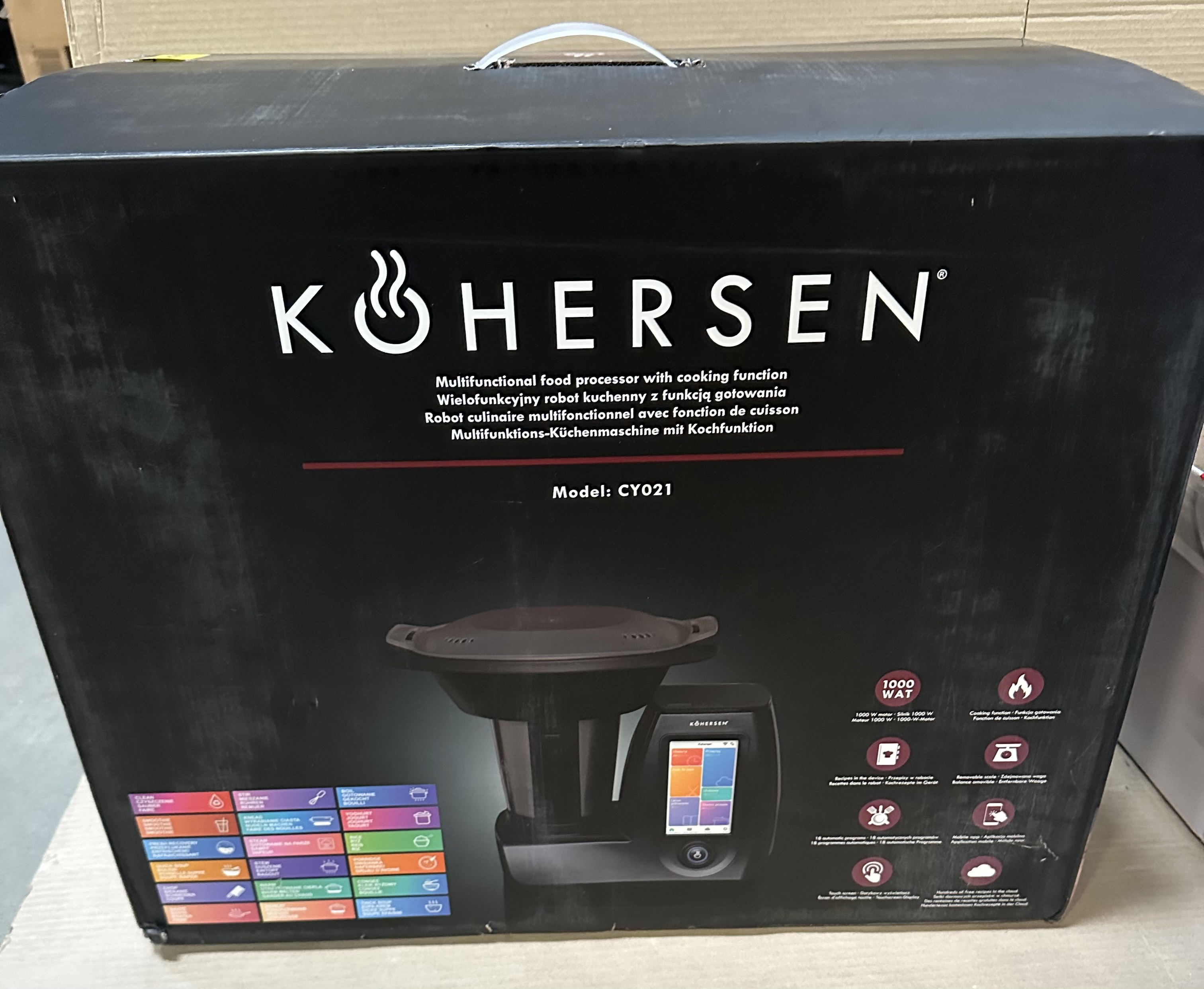 Czarne pudełko ze zdjęciem robota kuchennego i tekstem w różnych językach.