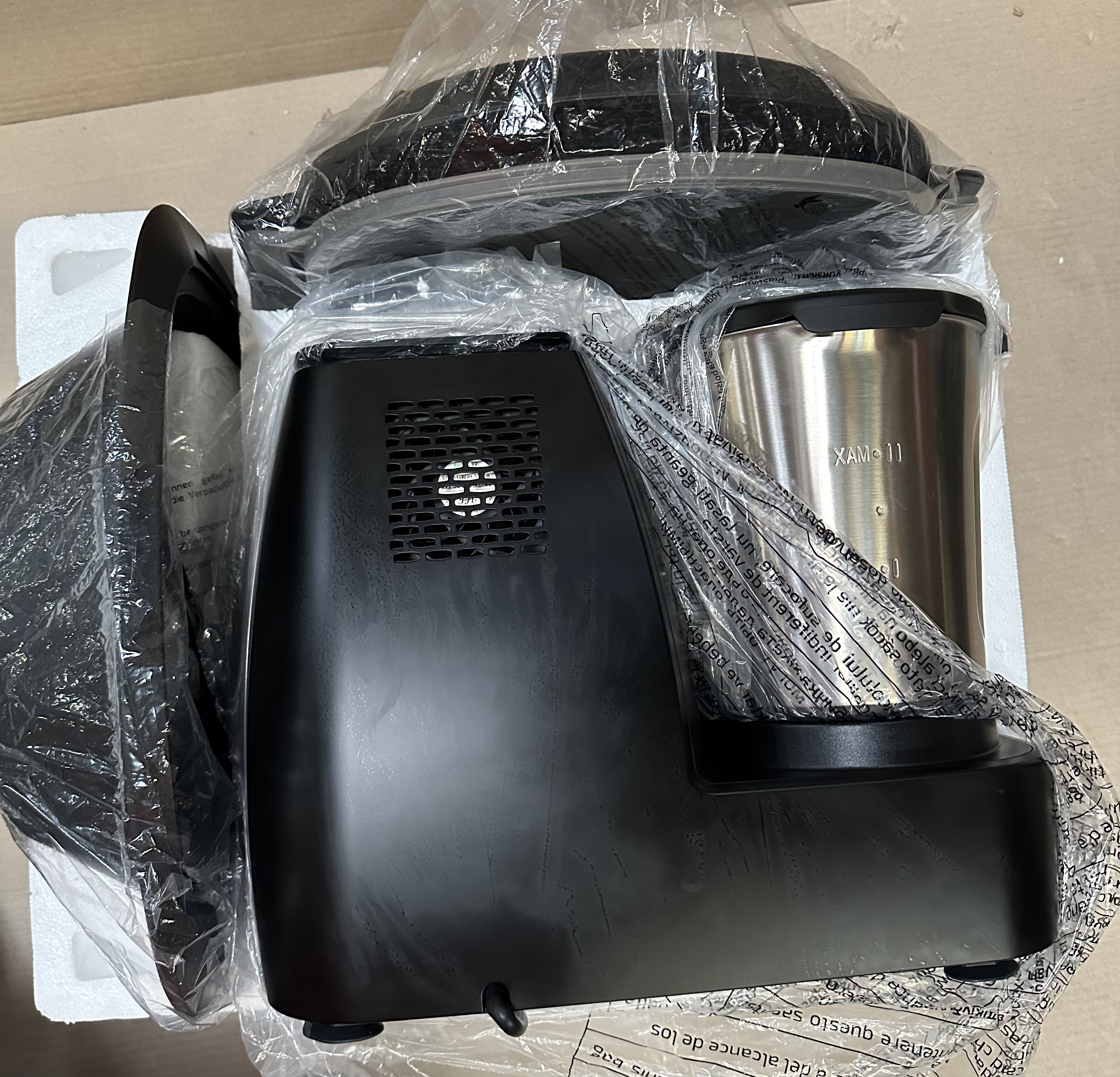 Czarne urządzenie kuchenne znajduje się w przezroczystej plastikowej torbie, z otwartą pokrywą.