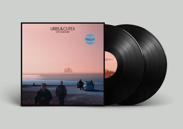 Albumcover mit zwei schwarzen Schallplatten. Das Cover zeigt eine Strandszene. Grauer Hintergrund.