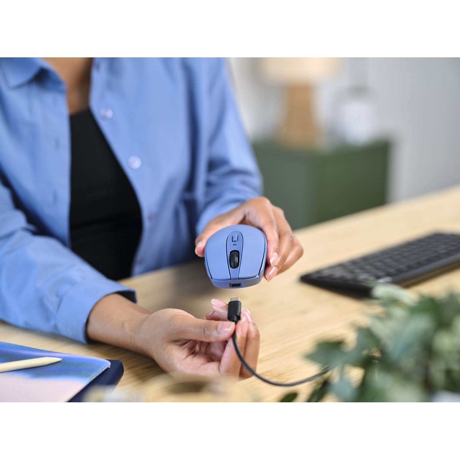 Persona che tiene un mouse blu, collegando un cavo USB-C. Tastiera e blocco note visibili.