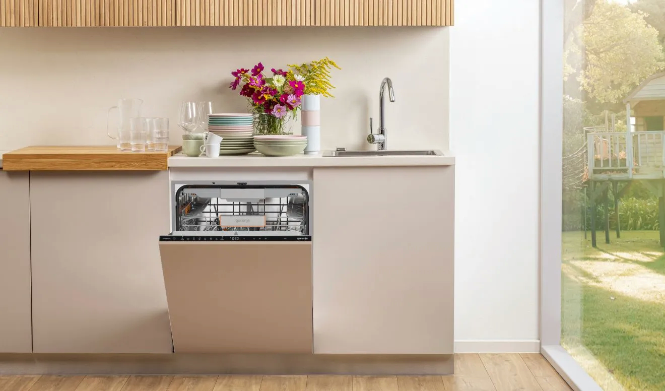 Eine Küchenszene mit einer geöffneten Gorenje-Spülmaschine, Blumen, Geschirr und Wasserhahn.