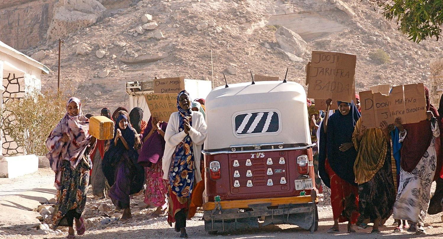 Eine Menschenmenge marschiert auf einer Straße und hält Schilder. Ein Tuk-Tuk steht in der Mitte.