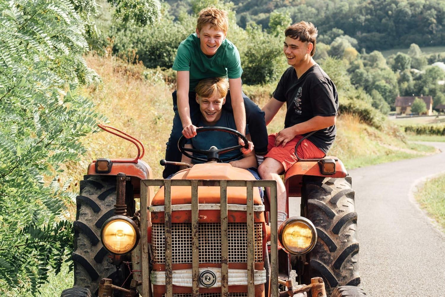 Drei Jungen auf einem Traktor. Einer fährt. Sie lächeln und schauen nach vorne.