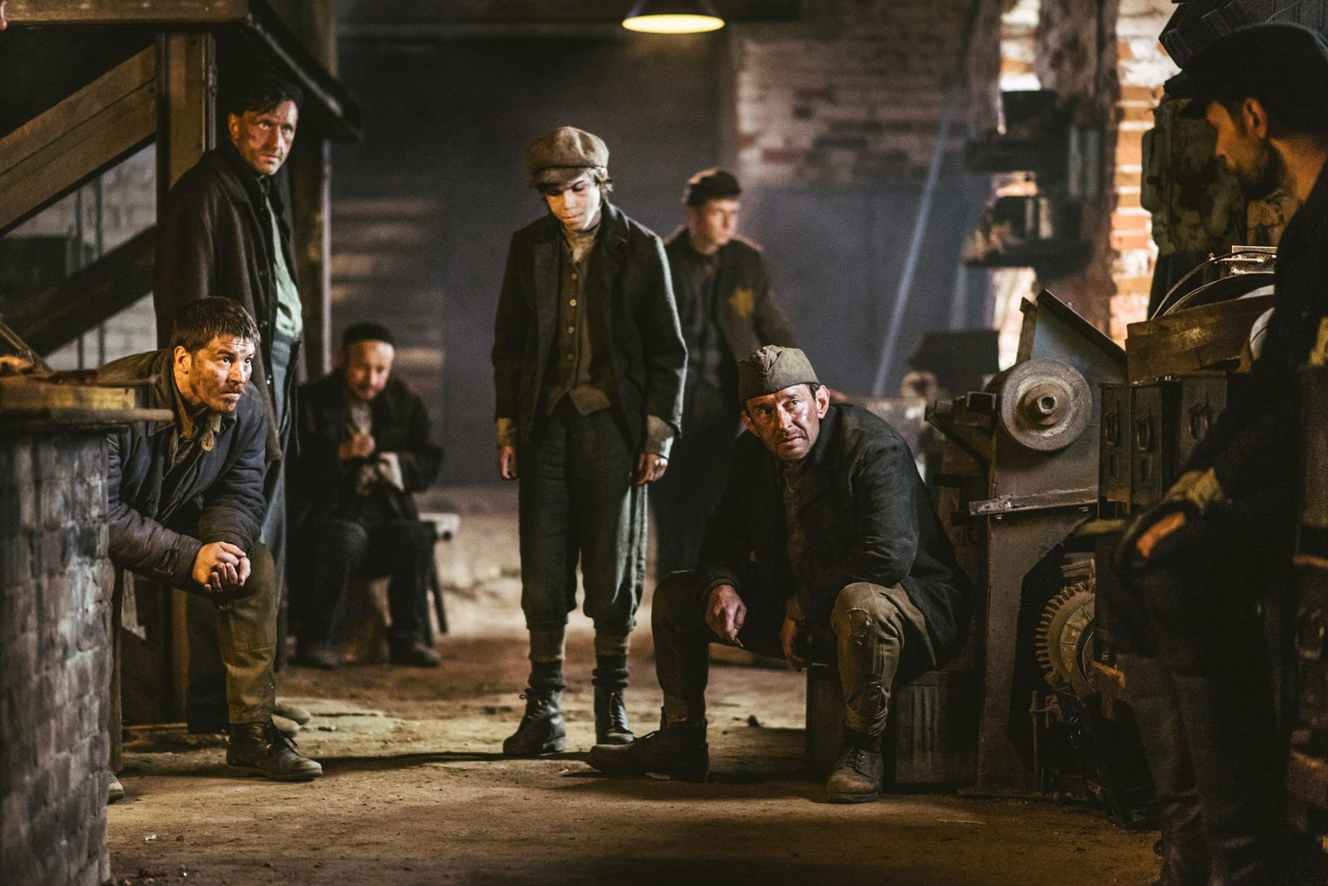 Eine Gruppe Männer in einem schwach beleuchteten Raum, wahrscheinlich eine Fabrik oder Werkstatt.