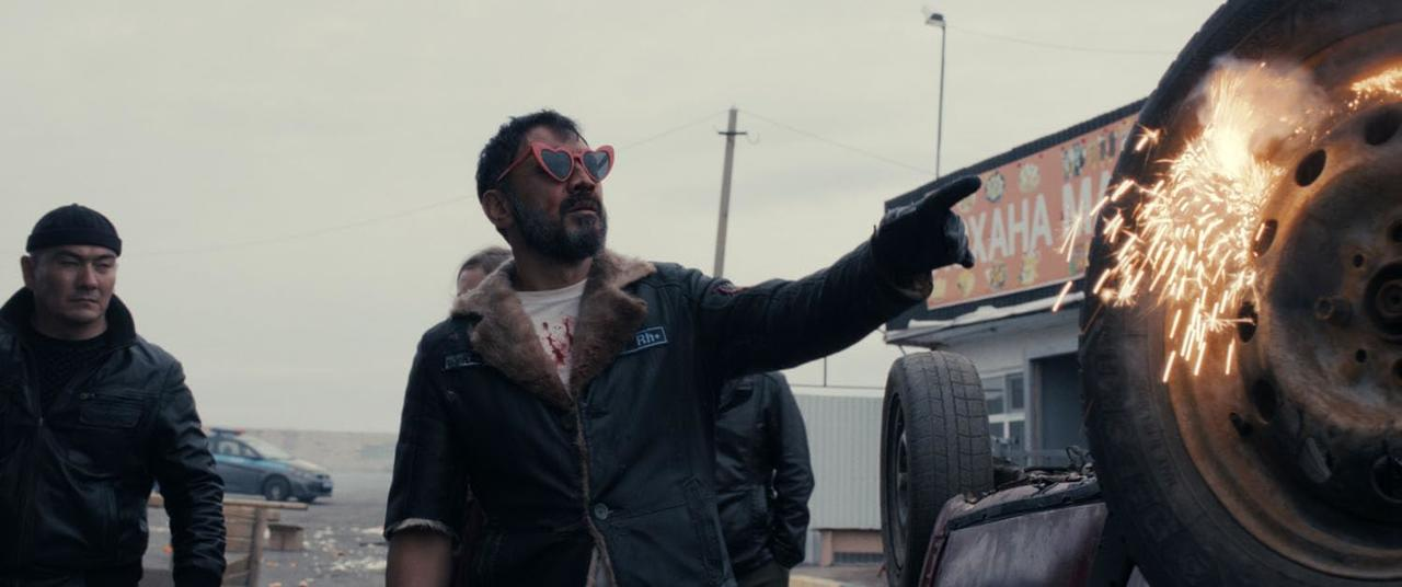 Ein Mann mit herzförmiger Sonnenbrille zeigt auf ein Autoreifen mit Funken.