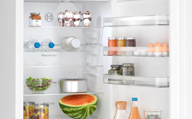 Refrigerador abierto con estantes de comida: botellas de agua, ensalada, frascos y sandía.