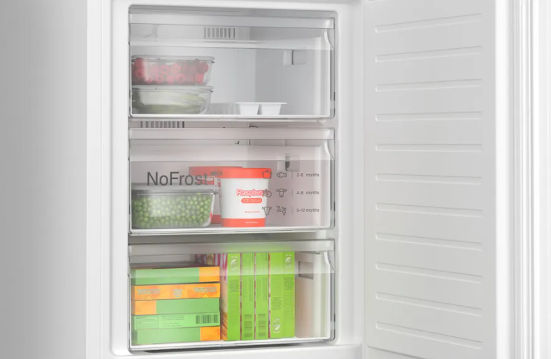 Un refrigerador abierto mostrando cajones de congelador llenos de alimentos como guisantes y frambuesas.