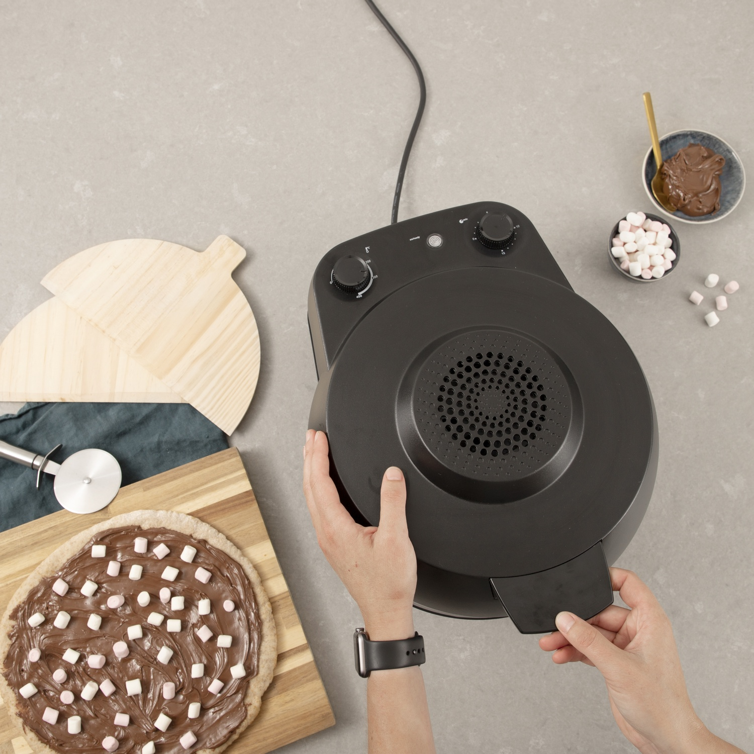Mani che tengono un coperchio di friggitrice ad aria nero, su un piano cucina con pizza.
