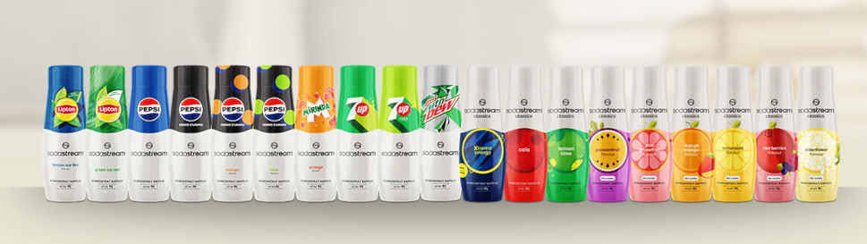 Wybór syropów SodaStream w wielu smakach. Znajdują się na białej powierzchni, są oznaczone i kolorowe.