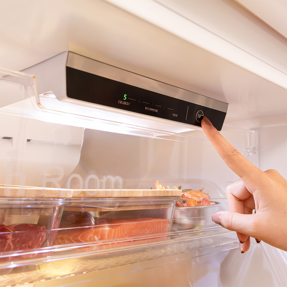Mano presionando el botón 'set' en el panel de control del refrigerador, con comida en estantes.