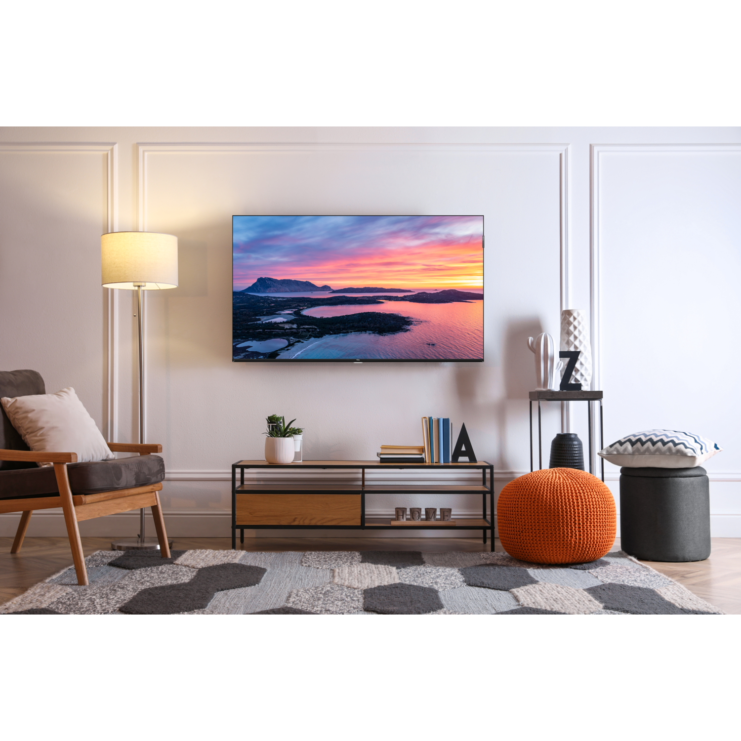 Salon avec une TV au mur, une lampe et un tapis à motifs.