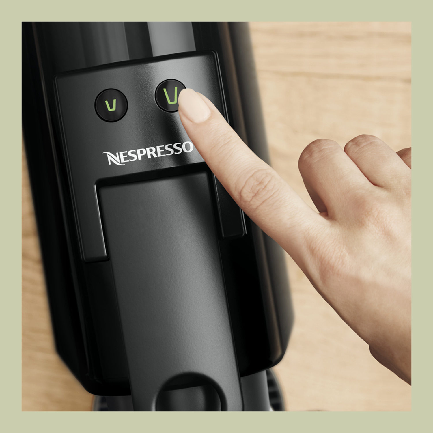 Close-up of a Nespresso machine, a finger pressing the green button. Black machine, wooden background.