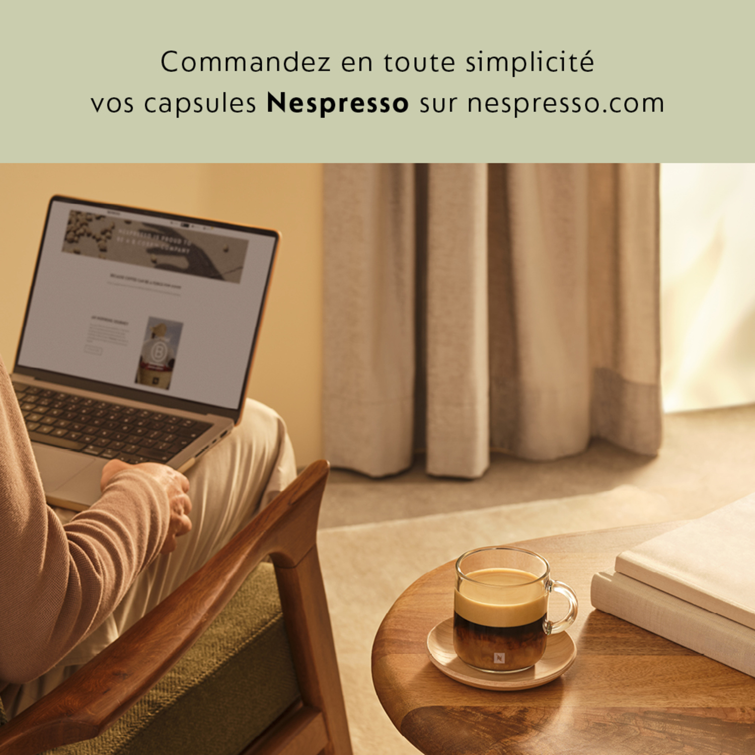 Personne utilisant un ordinateur portable, une tasse de café et un livre sur une table. Fenêtre et rideaux en arrière-plan.