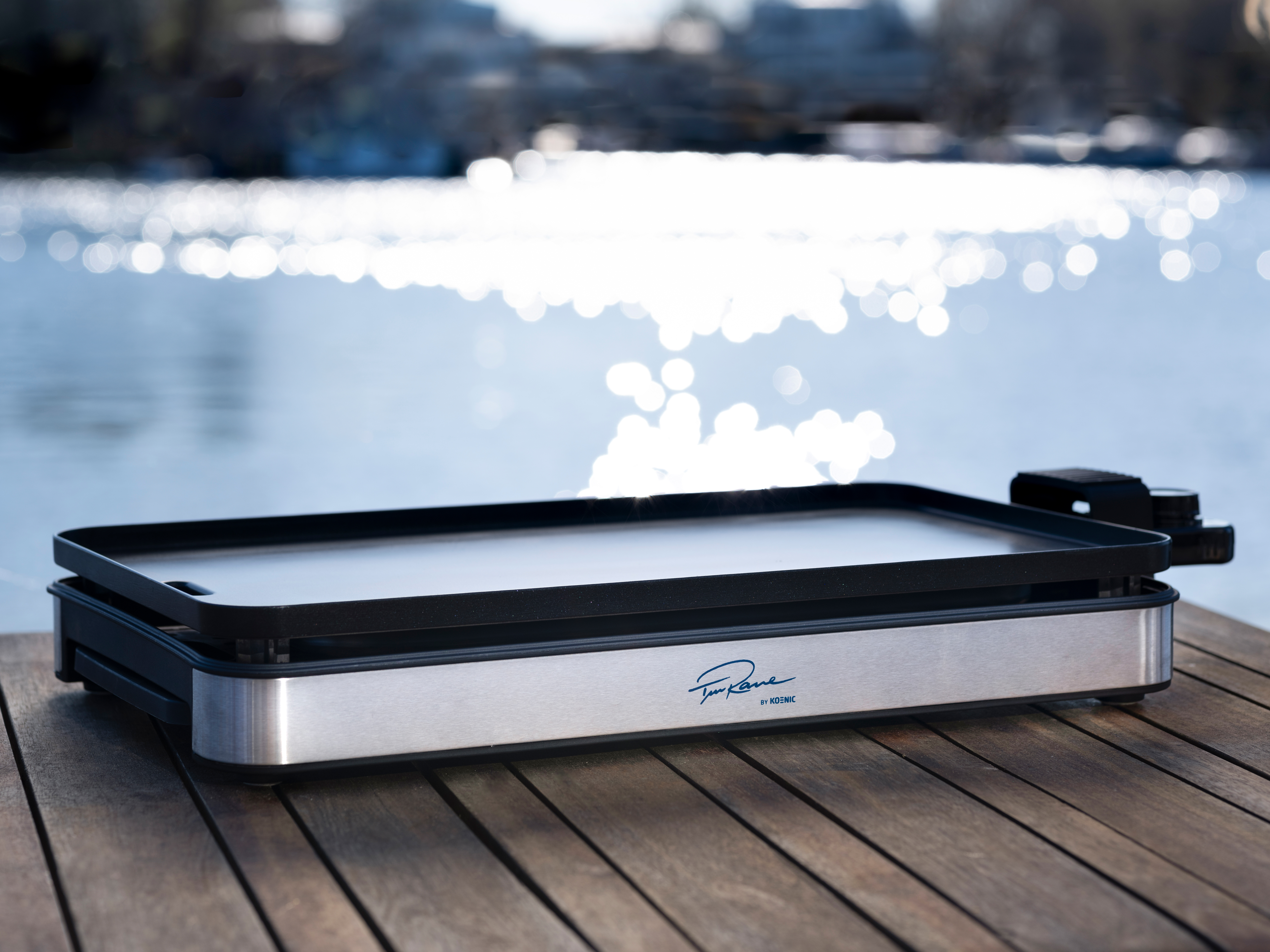 Ein Elektrogrill auf einer Holzoberfläche mit Wasserhintergrund.