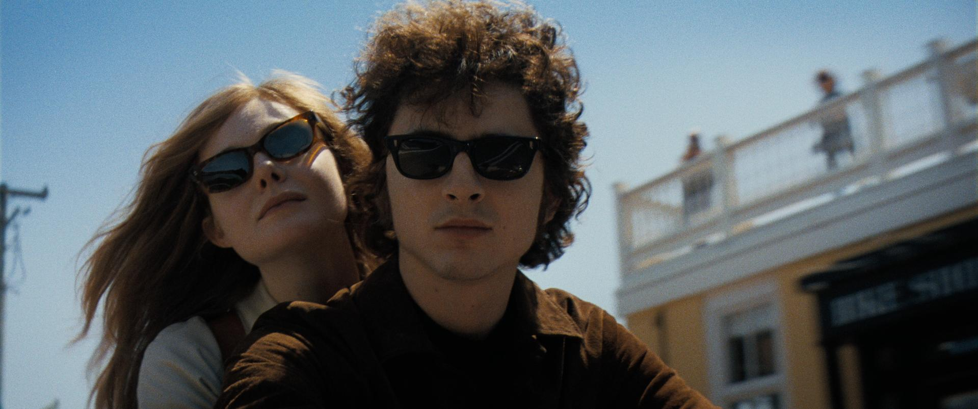 Ein Mann und eine Frau mit Sonnenbrille auf einem Motorrad. Der Hintergrund ist ein blauer Himmel.