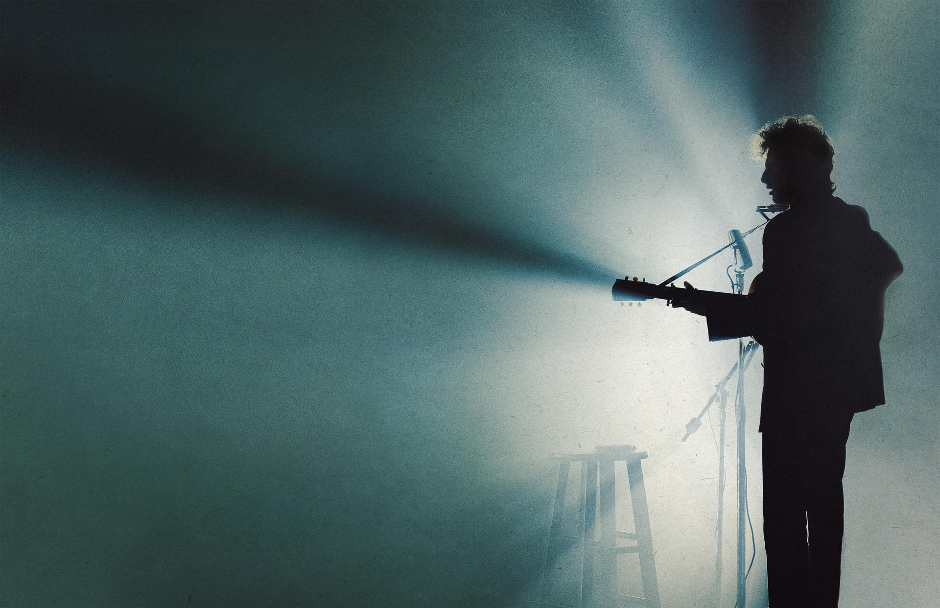 Silhouette eines Mannes, der auf der Bühne Gitarre spielt. Scheinwerfer leuchten ihn an. Hocker.