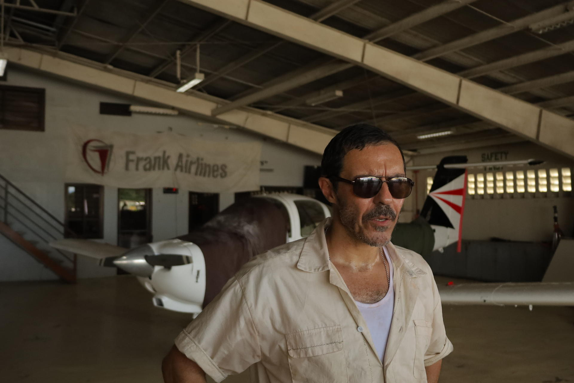 Mann mit Sonnenbrille vor Flugzeugen in einer Halle mit Frank Airlines Banner.
