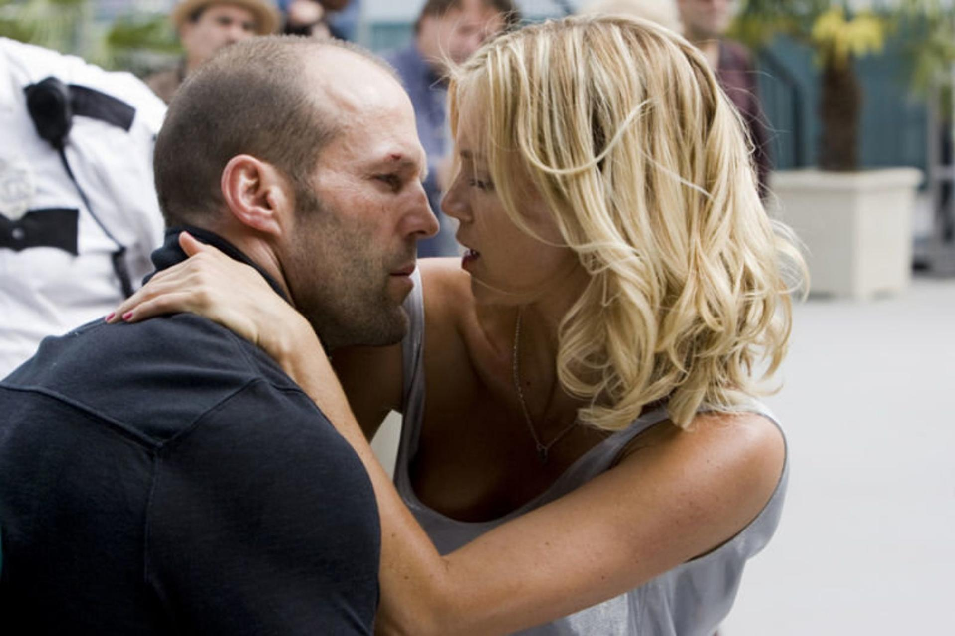 Ein Mann und eine Frau stehen sich nahe gegenüber. Die Frau hat blondes Haar. Der Mann hat einen rasierten Kopf. Andere Personen sind im Hintergrund.