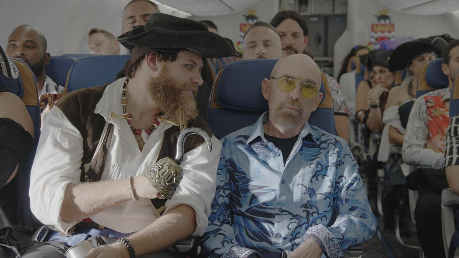 Pirat mit Hakenhand und Mann im blauen Hemd im Flugzeug. Andere Passagiere sind im Hintergrund sichtbar.