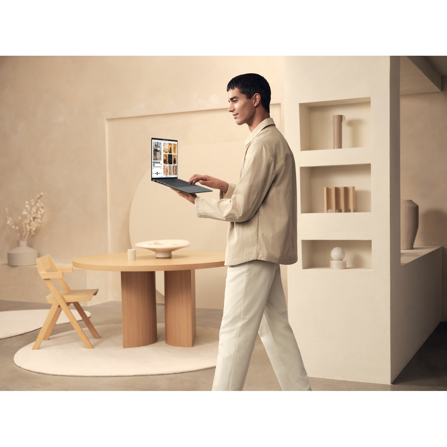 Un uomo tiene un laptop, camminando in un interno moderno con una palette di colori neutri.