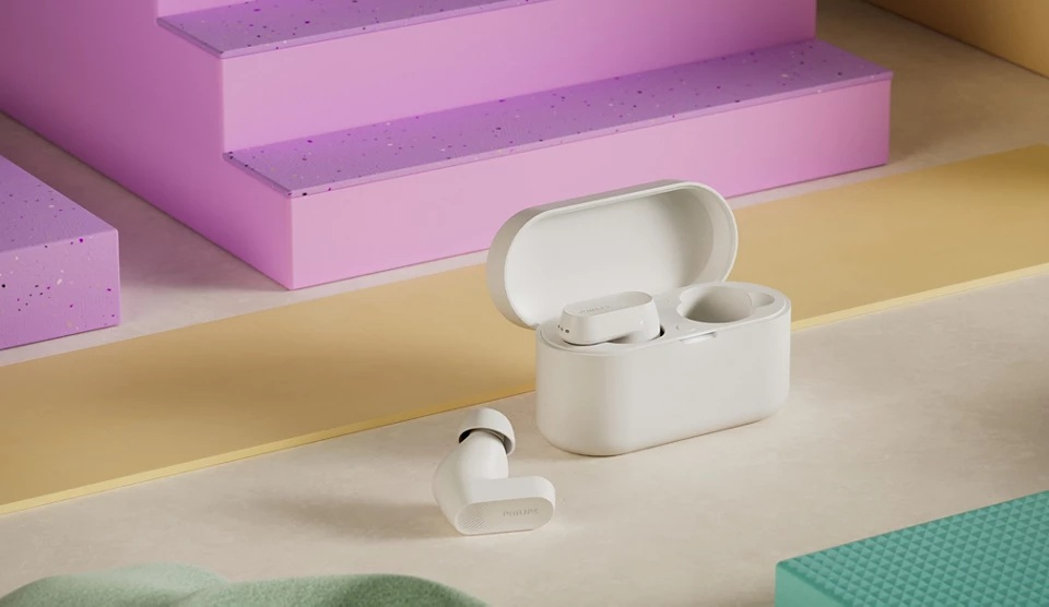 Białe etui ładujące, słuchawki i jedna słuchawka leżą na powierzchni z geometrycznymi kształtami w tle.