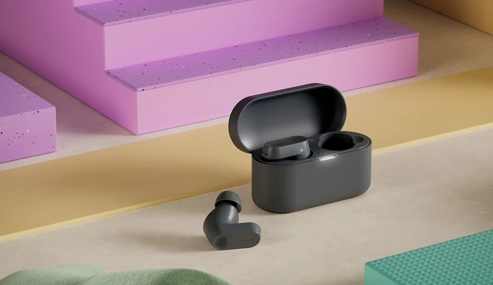 Bezprzewodowe szare słuchawki i etui ładujące na powierzchni z pastelowym tłem.