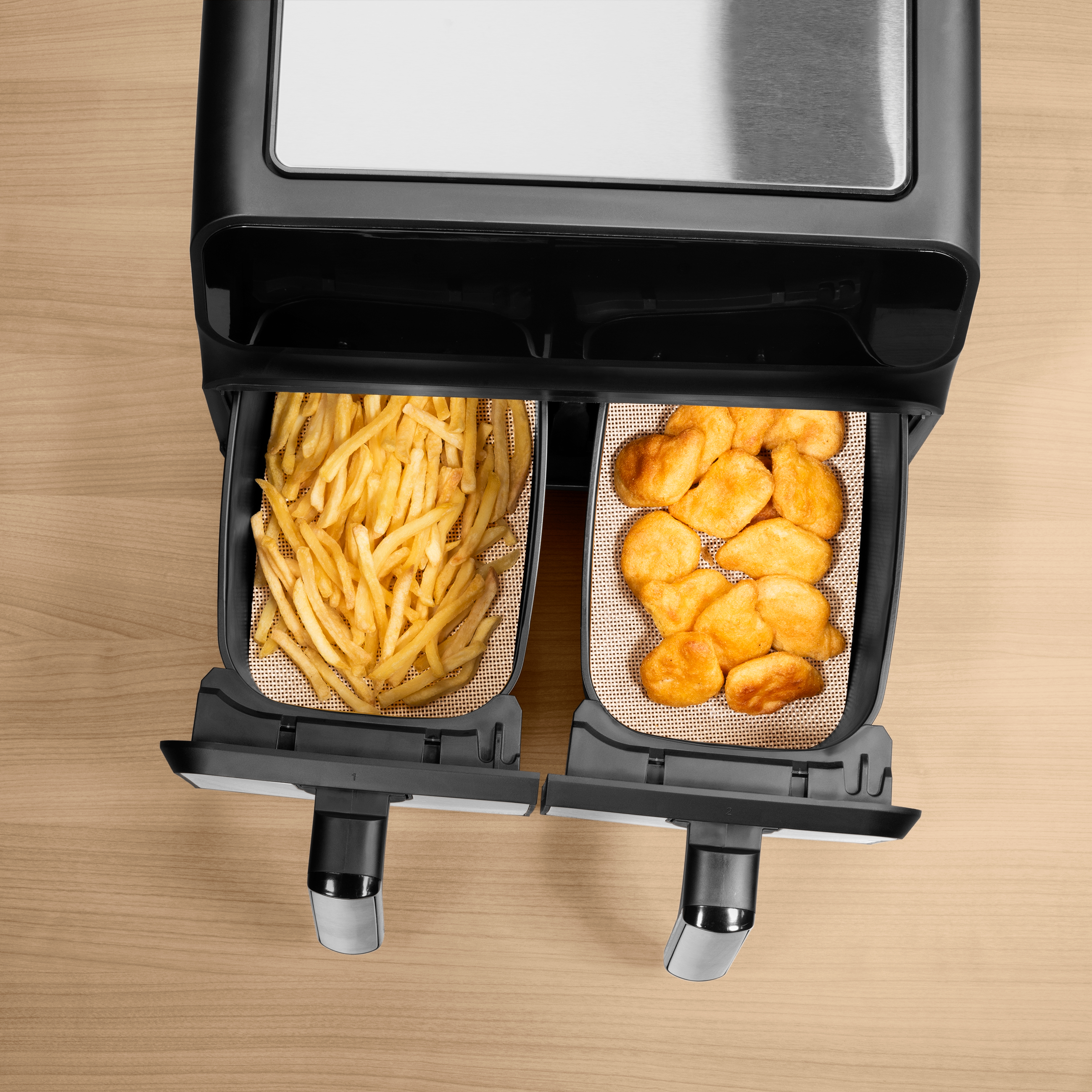 Eine Heißluftfritteuse mit zwei Körben, einem mit Pommes und einem mit Nuggets, auf Holzoberfläche.