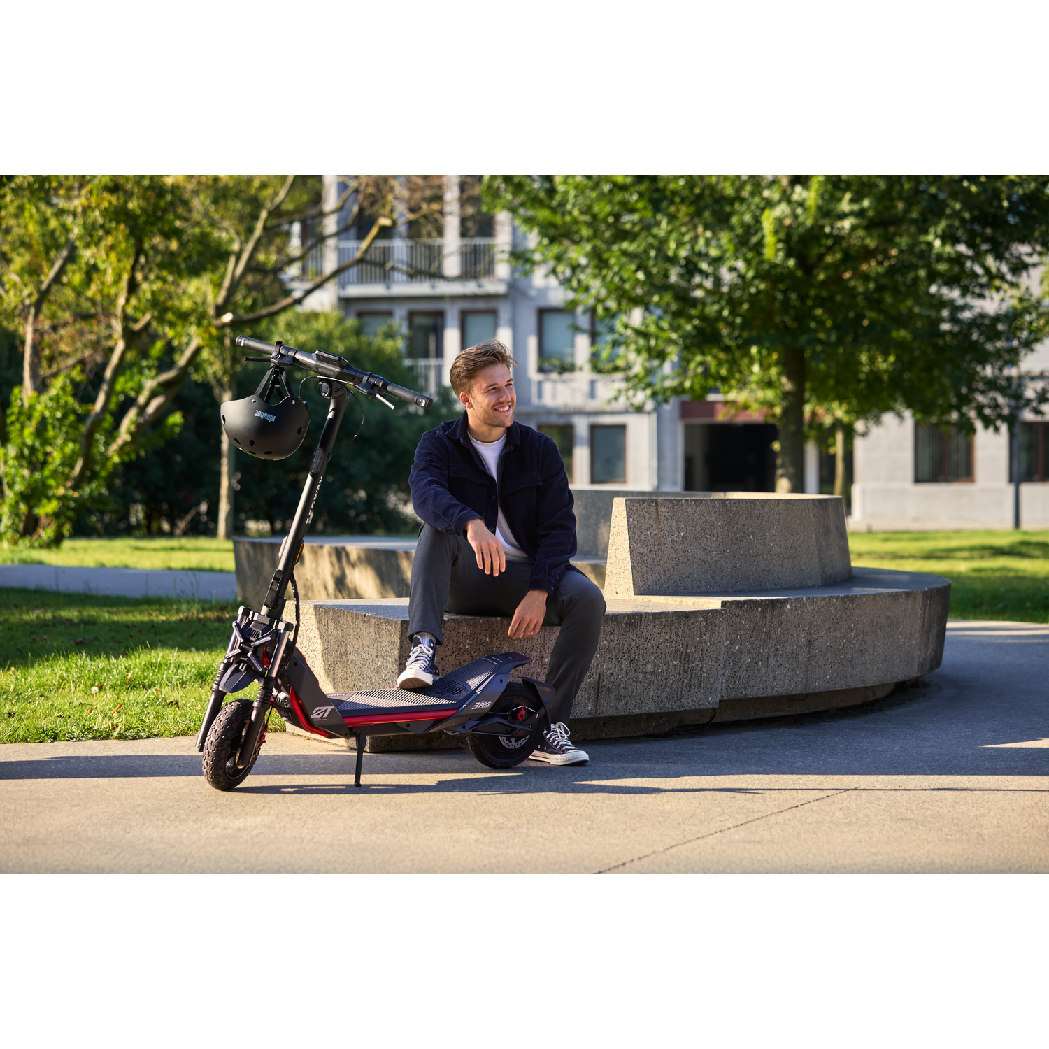 Homme blond assis sur un banc avec une trottinette électrique.