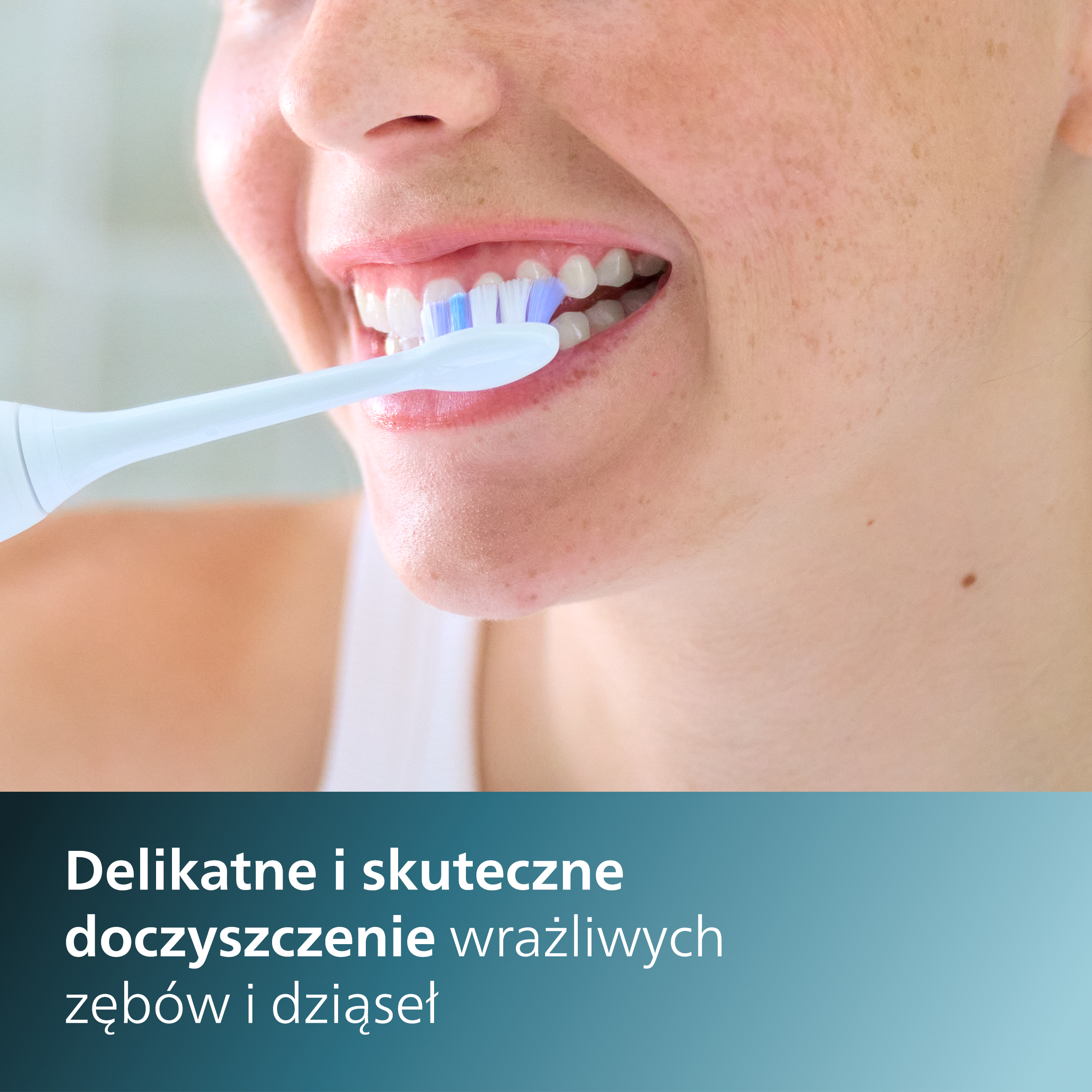 Kobieta myje zęby szczoteczką elektryczną. Tekst: Delikatne i skuteczne doczyszczenie wrażliwych zębów i dziąseł.