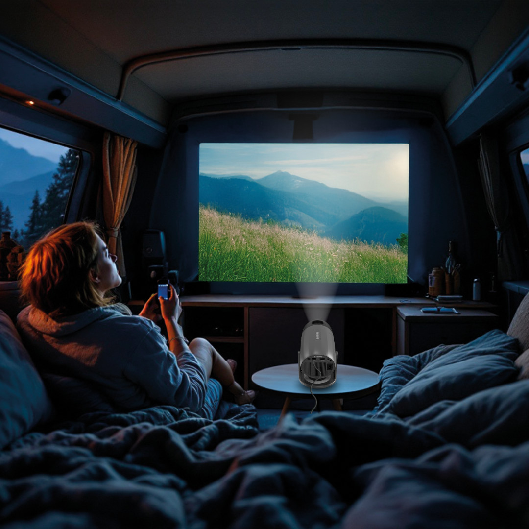 Kobieta ogląda film na ekranie w vanie. Projektor stoi na stole.