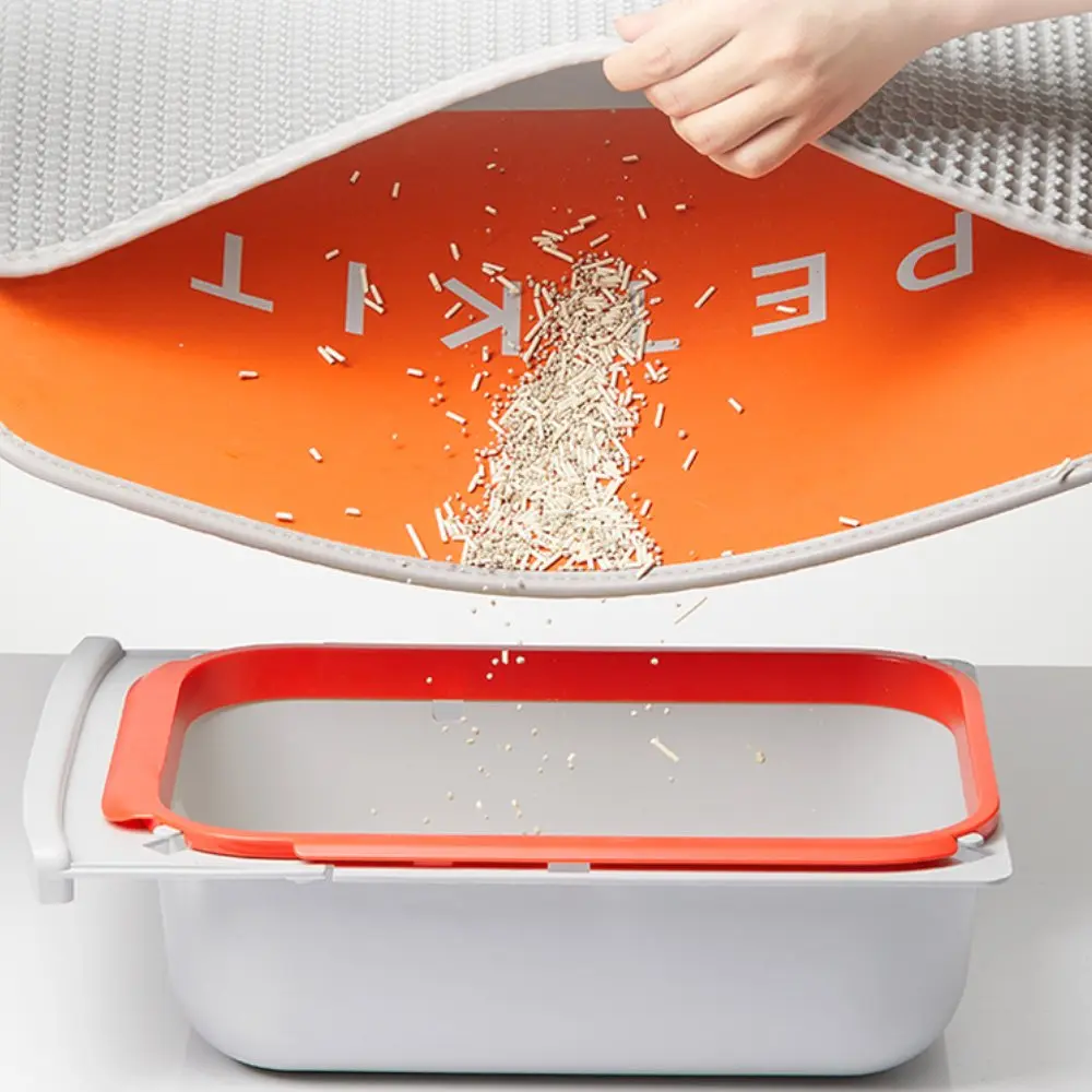 Main lève tapis gris, litière tombe sur un bac orange.