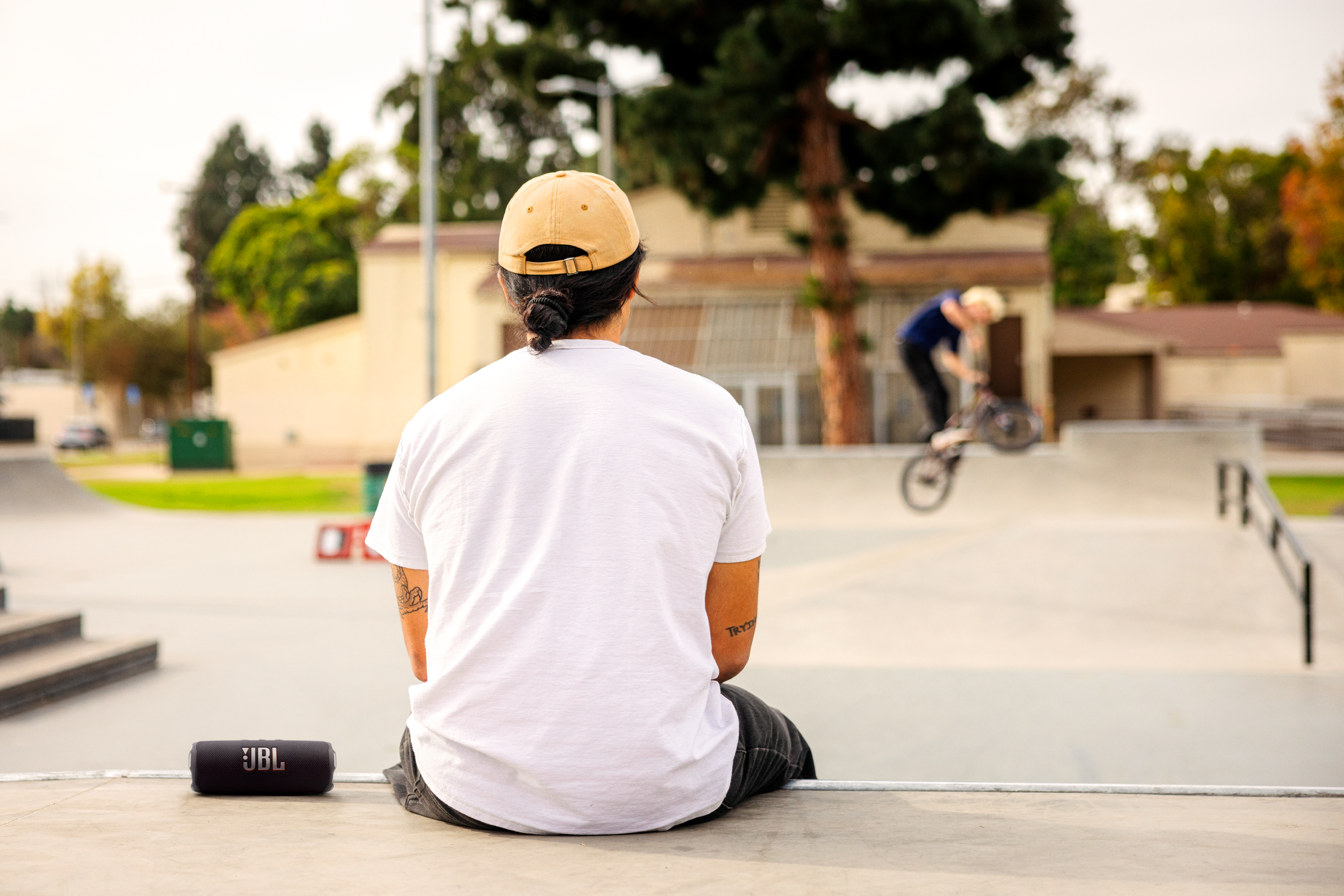 Bir adam hoparlörün yanında oturmuş, bir BMX binicisini izliyor.